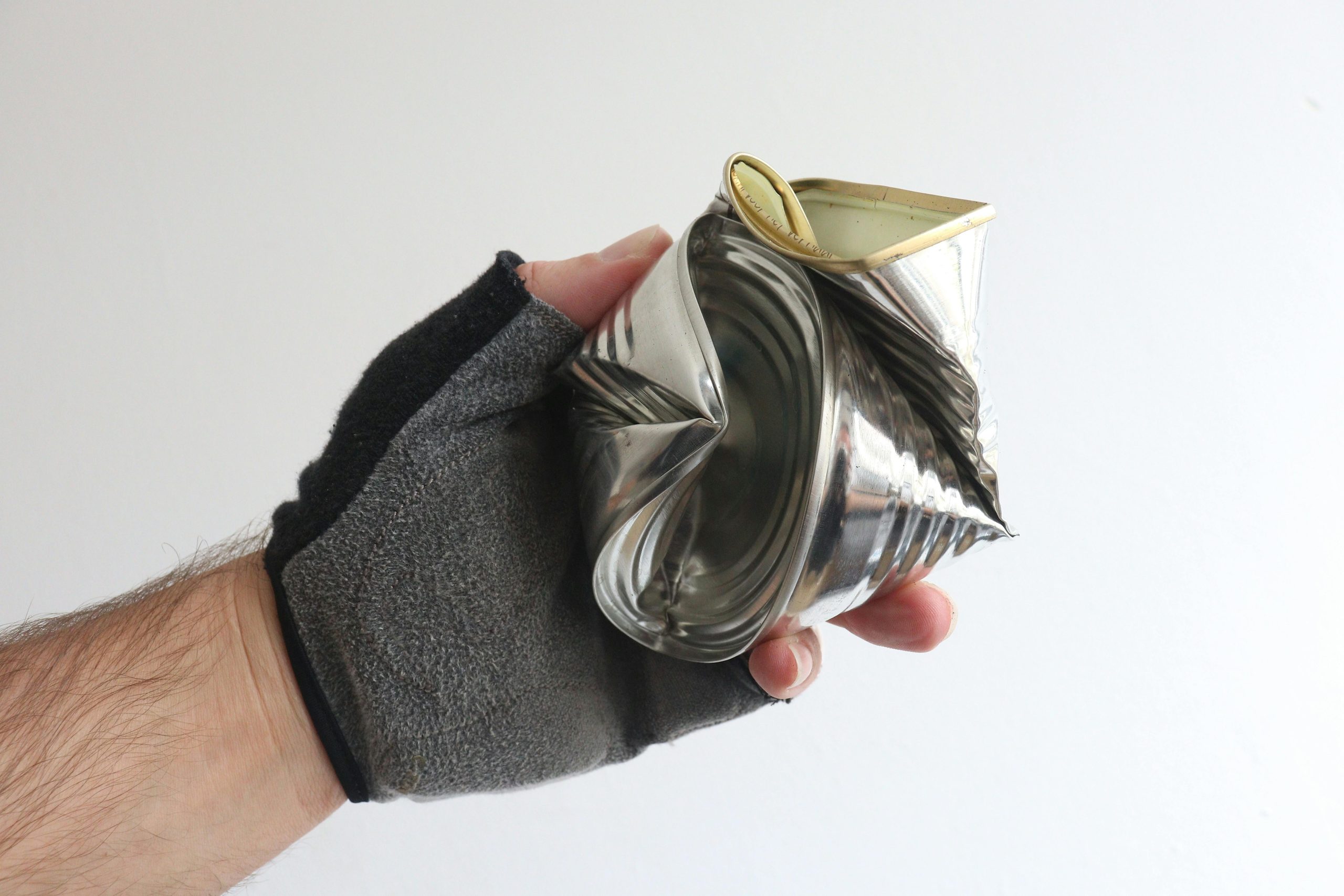 A gloved hand holding a crushed tin can showcases recycling and waste management.