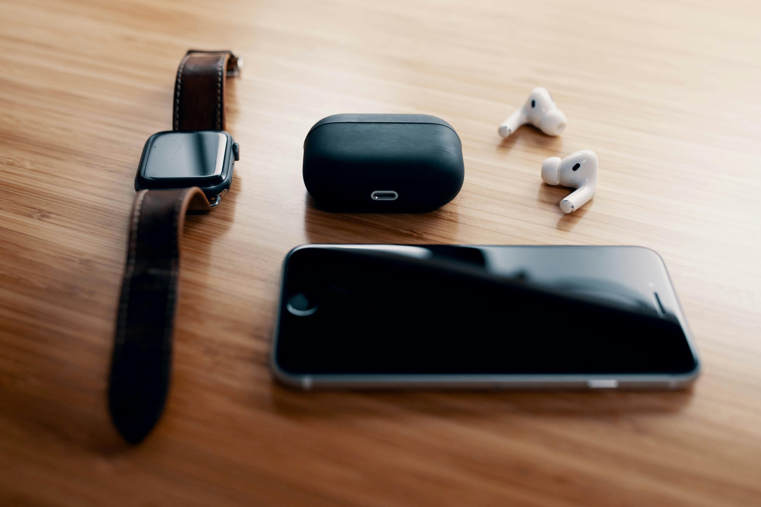 Black smart watch and TWS earbuds with charging case and smartphone lying on wooden table