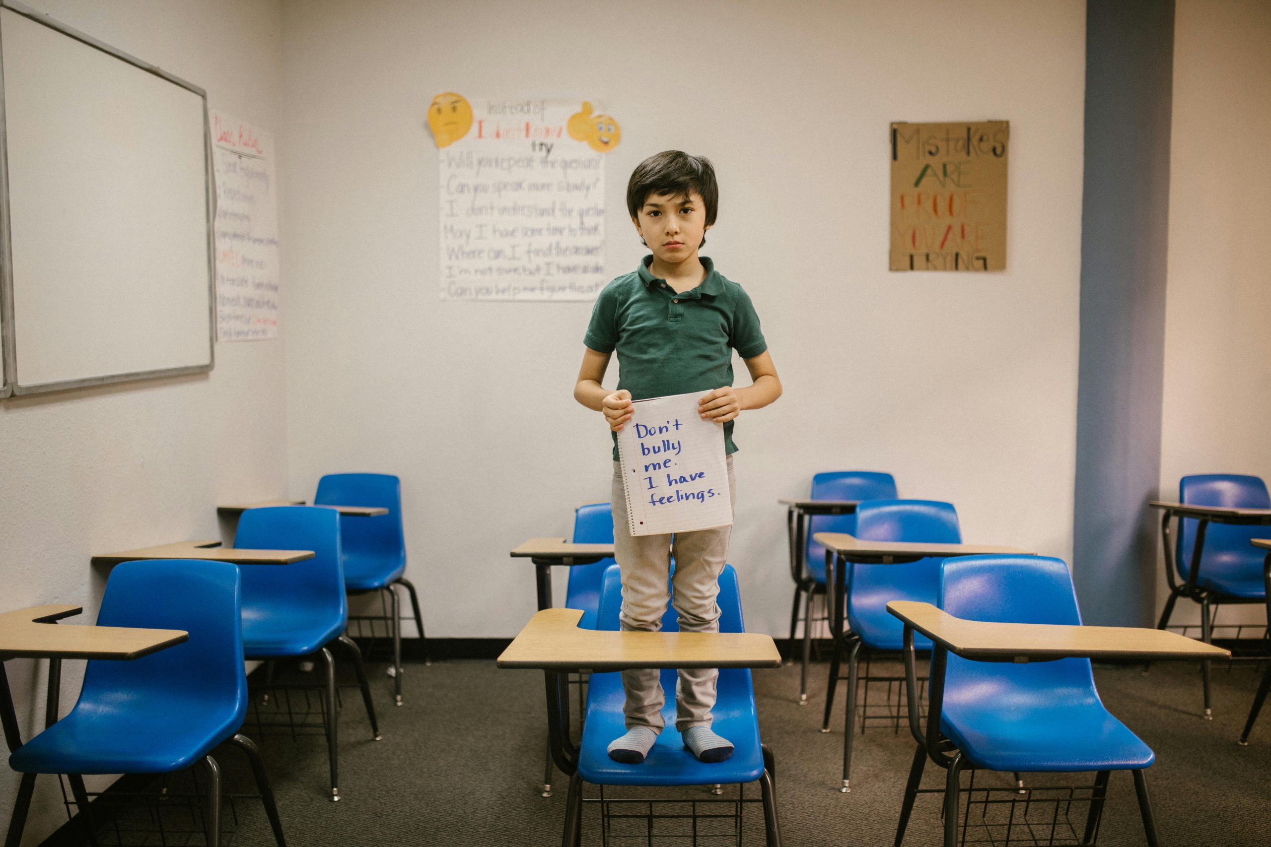 Child standing on desk in classroom holding a sign against bullying, promoting kindness and awareness.