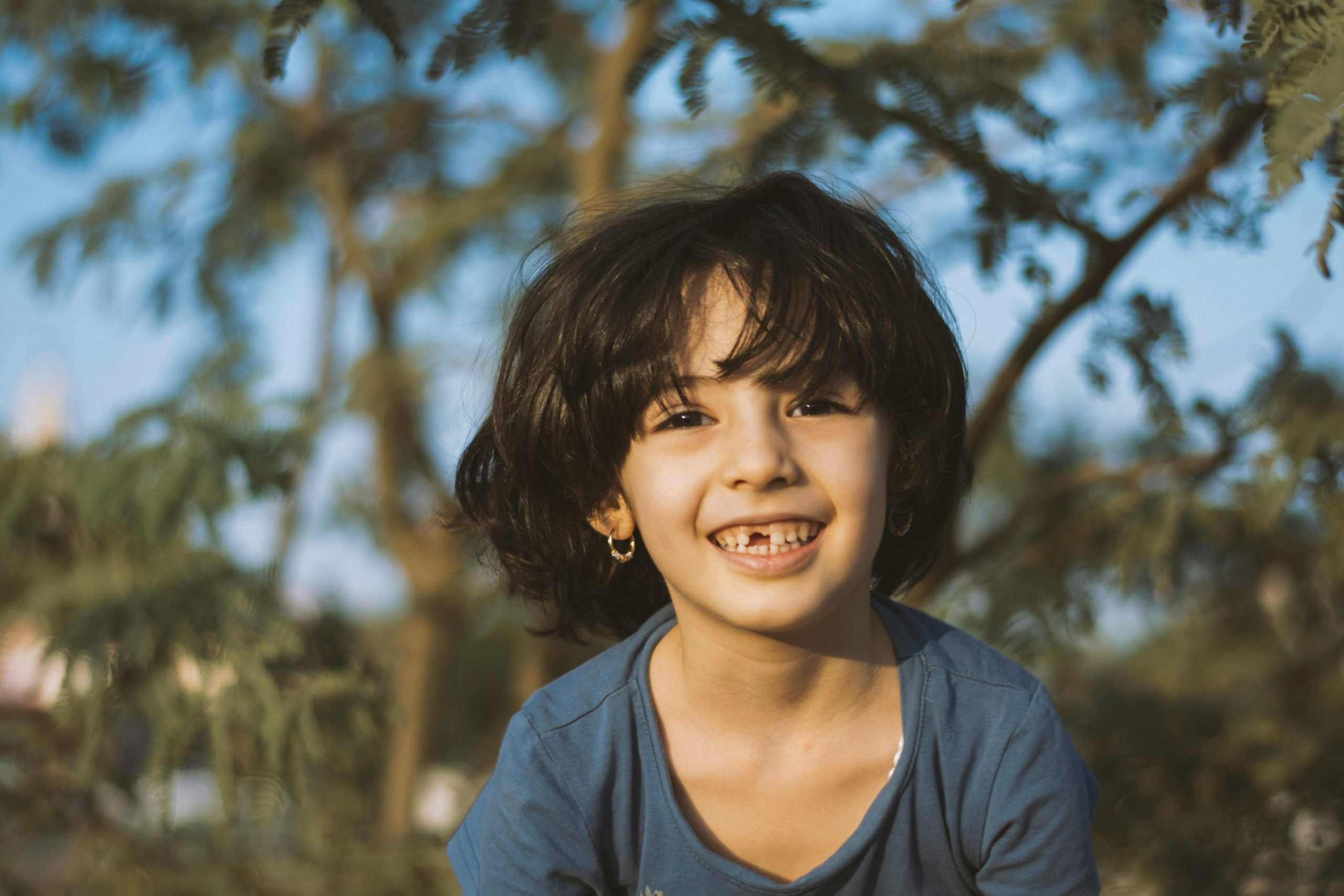 Joyful child smiling brightly in a sunny outdoor setting, surrounded by nature.
