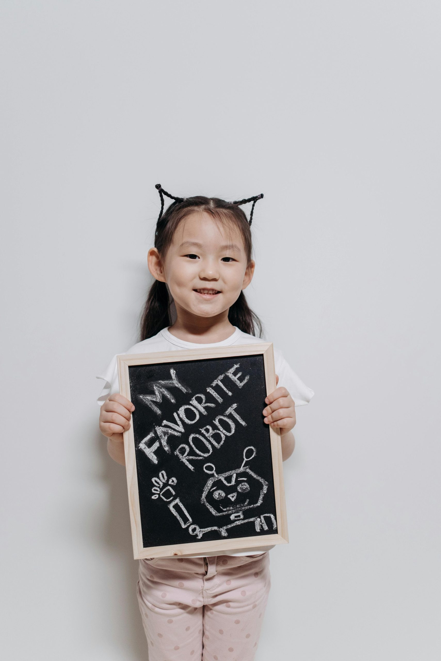 Cheerful girl holding a chalkboard with a robot drawing on a white background.
